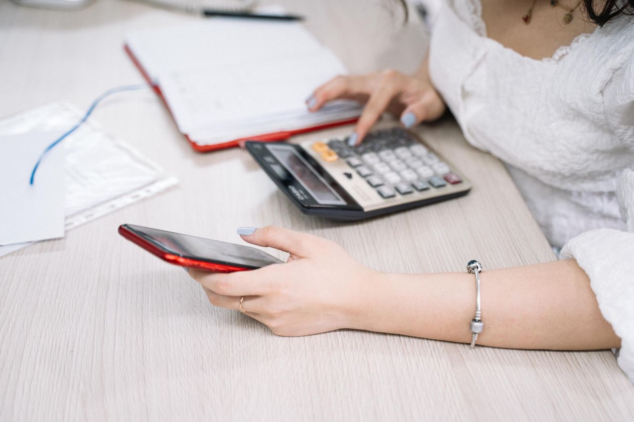 A woman managing finances using a calculator and smartphone at her desk, showcasing multitasking in an office setting.