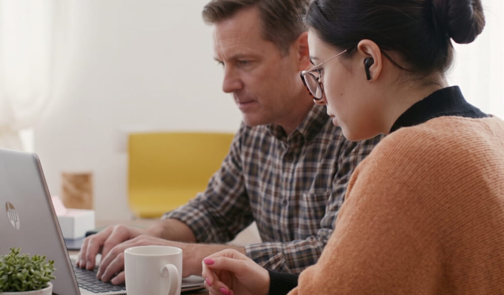 A diverse team of four employees collaborative planning a work schedule using a large touchscreen device in a modern office, visualizing the results of an online shift generator to replace an old paper spreadsheet.